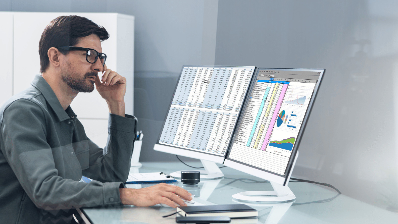 Banking executive sitting at desk staring at spreadsheets on two computer monitors