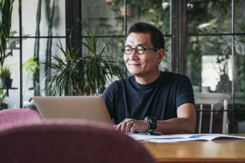 Mature man in glasses at home, typing on computer, contented, small business owner